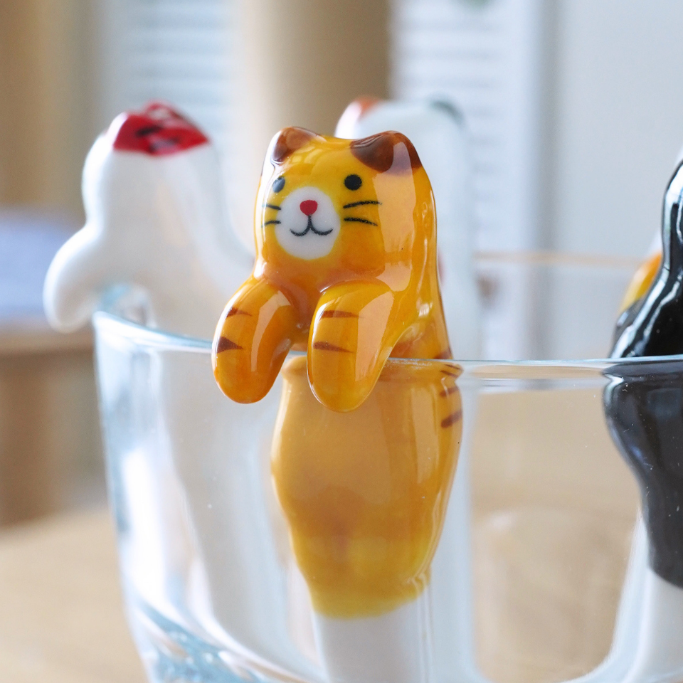 Three small cat-shaped novelty items resting in a clear glass on a wooden table, with a softly blurred indoor background.