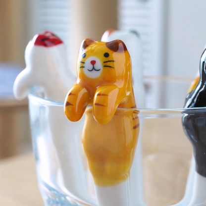 Three small cat-shaped novelty items resting in a clear glass on a wooden table, with a softly blurred indoor background.