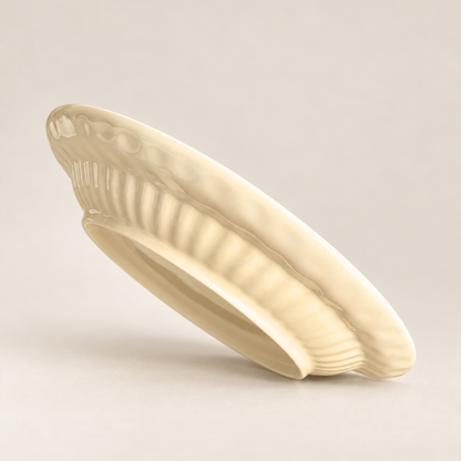 An off-white ceramic plate with a ribbed, scalloped edge, shown at an angle on a neutral light beige background.