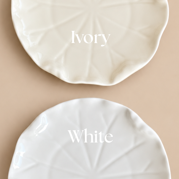 Two round ceramic plates with a leaf-like radial pattern, shown on a beige background. The top plate is labeled 'Ivory' and appears warm off-white, while the bottom plate is labeled 'White' and appears bright white.