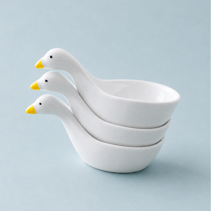 Three stacked white ceramic duck-shaped bowls with yellow beaks on a light blue background.