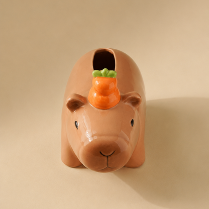 A glossy ceramic capybara-shaped tissue cover with a small orange yuzu on its back, set against a solid beige background.