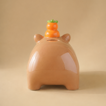 A glossy ceramic capy-shaped tissue cover in a warm tan-brown color, featuring a small yuzu topper with green leaves on its back, set against a solid beige background.
