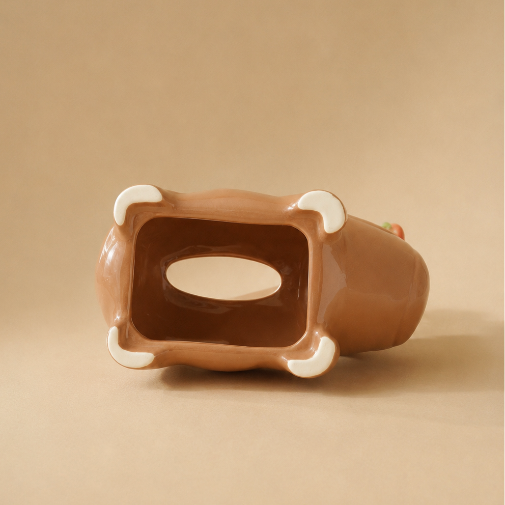 A brown ceramic animal-shaped capybara tissue holder, shown from a top-down view, featuring white accents on its paws and a matching brown interior with a central oval cutout, set against a solid beige background.
