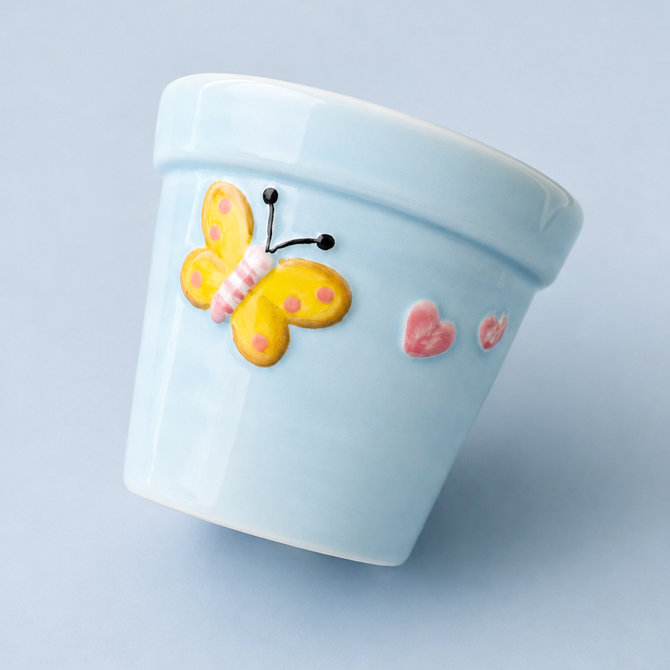 A light blue ceramic planter pot decorated with a yellow and pink butterfly and small pink hearts, shown on a solid light blue background.