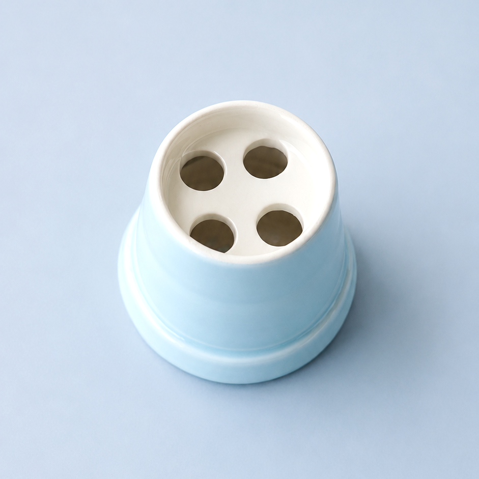 A light blue and white ceramic cup with four drainage holes, photographed from a top-down perspective on a solid light blue background.