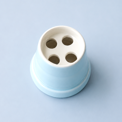 A light blue and white ceramic cup with four drainage holes, photographed from a top-down perspective on a solid light blue background.