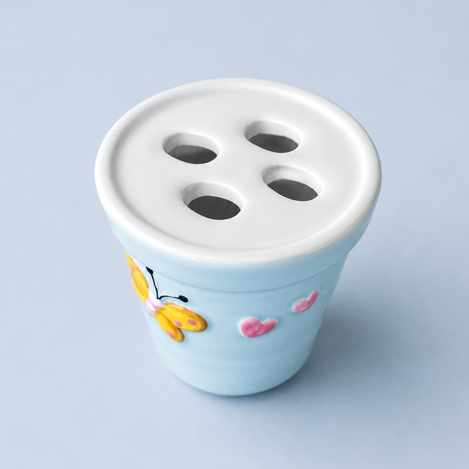 A light blue ceramic measuring spoon holder with a white top featuring four circular holes, decorated with a yellow butterfly and pink hearts on the side, set against a solid light blue background.