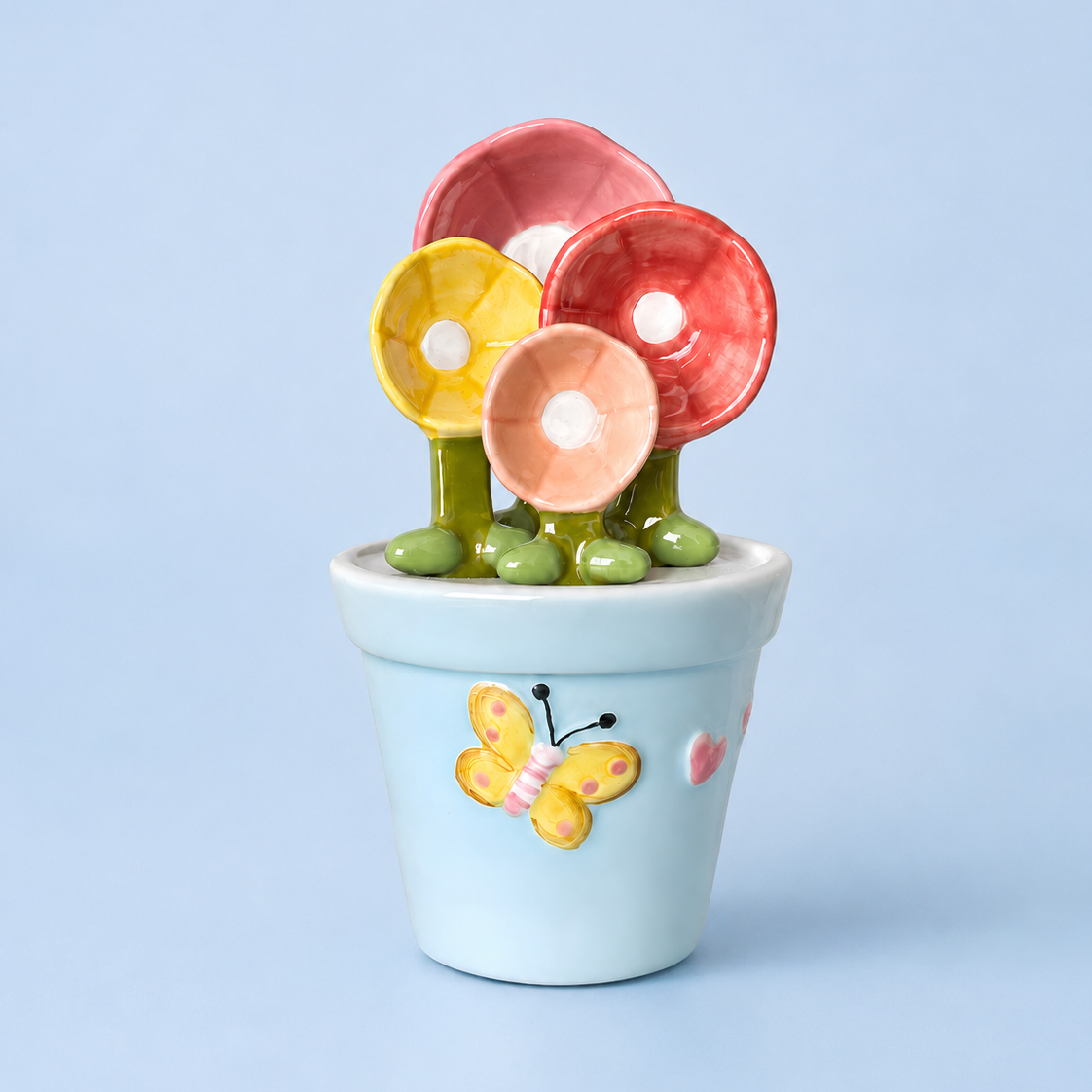 A ceramic flower pot figurine with three colorful flowers (yellow, pink, and red) on green stems, set against a solid light blue background.
