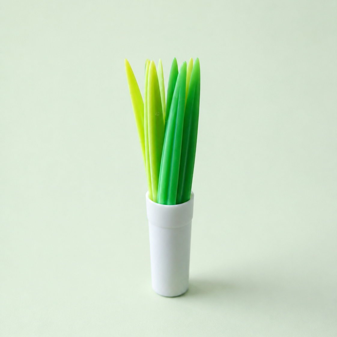 A set of pointed green and yellow snack picks standing upright in a small white cylindrical holder against a pale mint-green background.