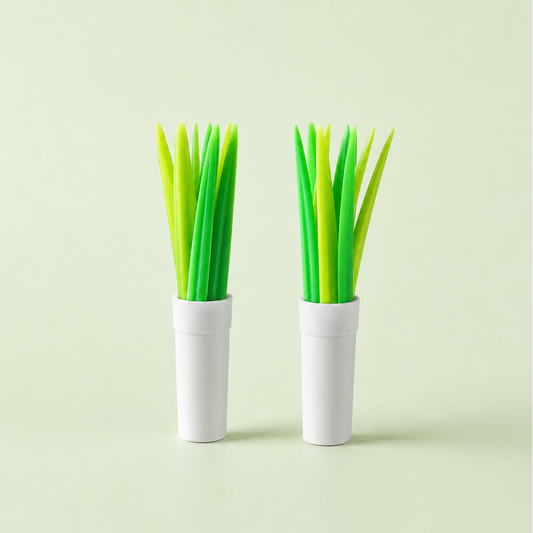 Two white cylindrical holders containing bright green and yellow grass-shaped decorative snack picks, set against a solid pale green background.