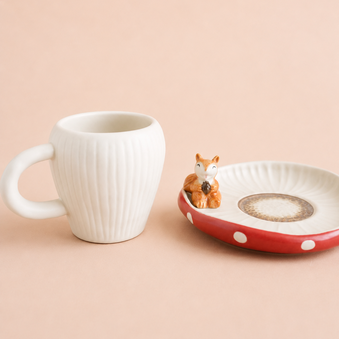 A white ribbed ceramic mug and a red-and-white ceramic dish with a small squirrel figurine, set against a solid pale peach background.