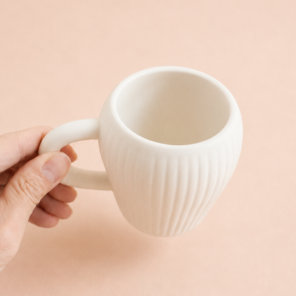 A hand holding a white ceramic mug with a ribbed vertical texture against a solid pale peach background.