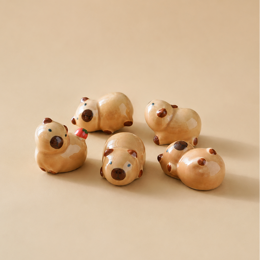 Five small ceramic animal capybara figurines in a warm beige glaze, arranged on a plain beige background.