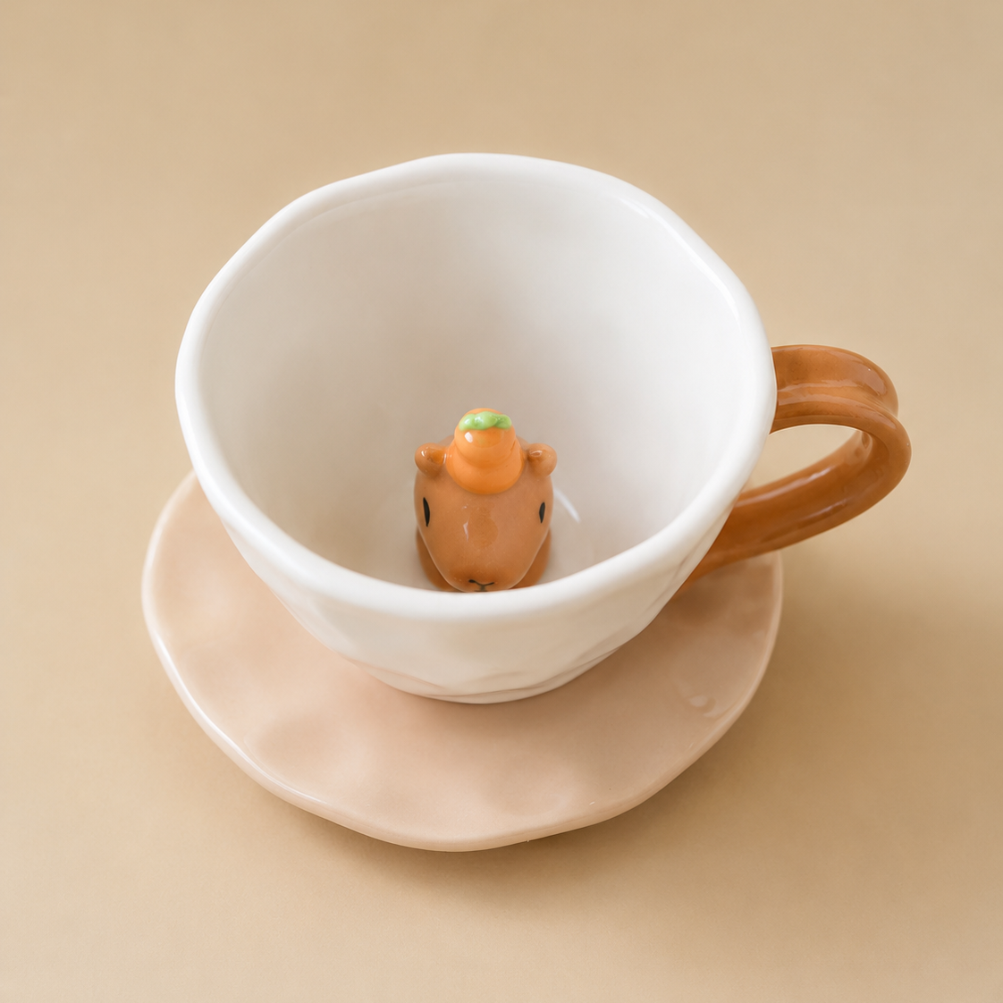 Top view of a white ceramic capybara teacup and matching beige saucer, showing the 3D capybara head with a miniature orange yuzu and green leaf inside.