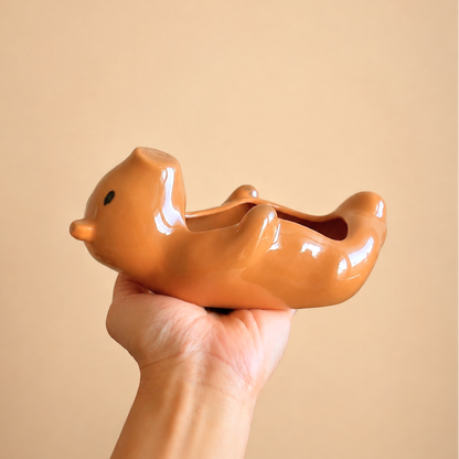 A glossy ceramic capybara-shaped planter held in a person's hand against a solid beige background.