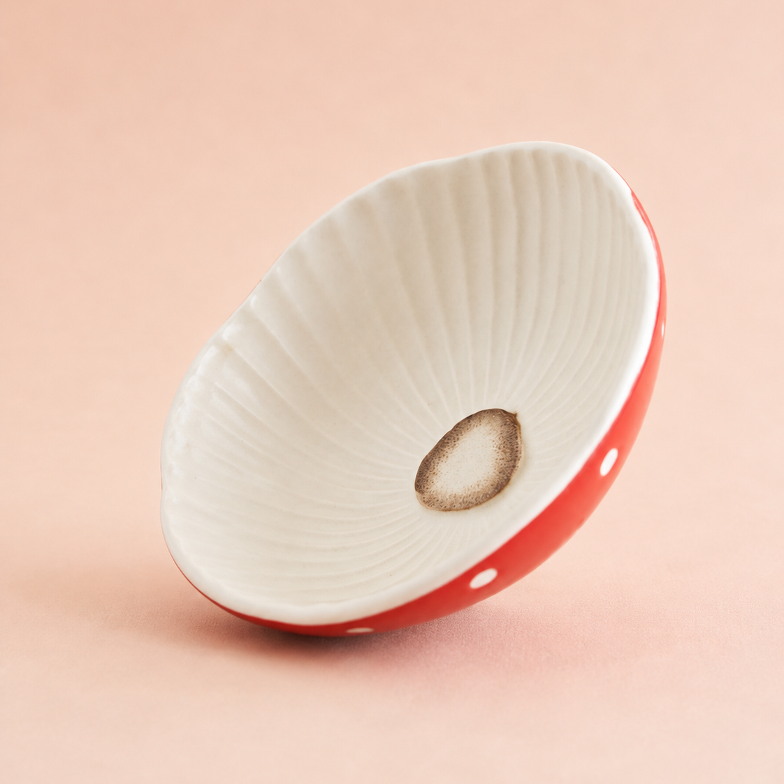 A small ceramic dish or bowl with a white ribbed interior and a red exterior decorated with white polka dots, shown on a solid peach-pink background.