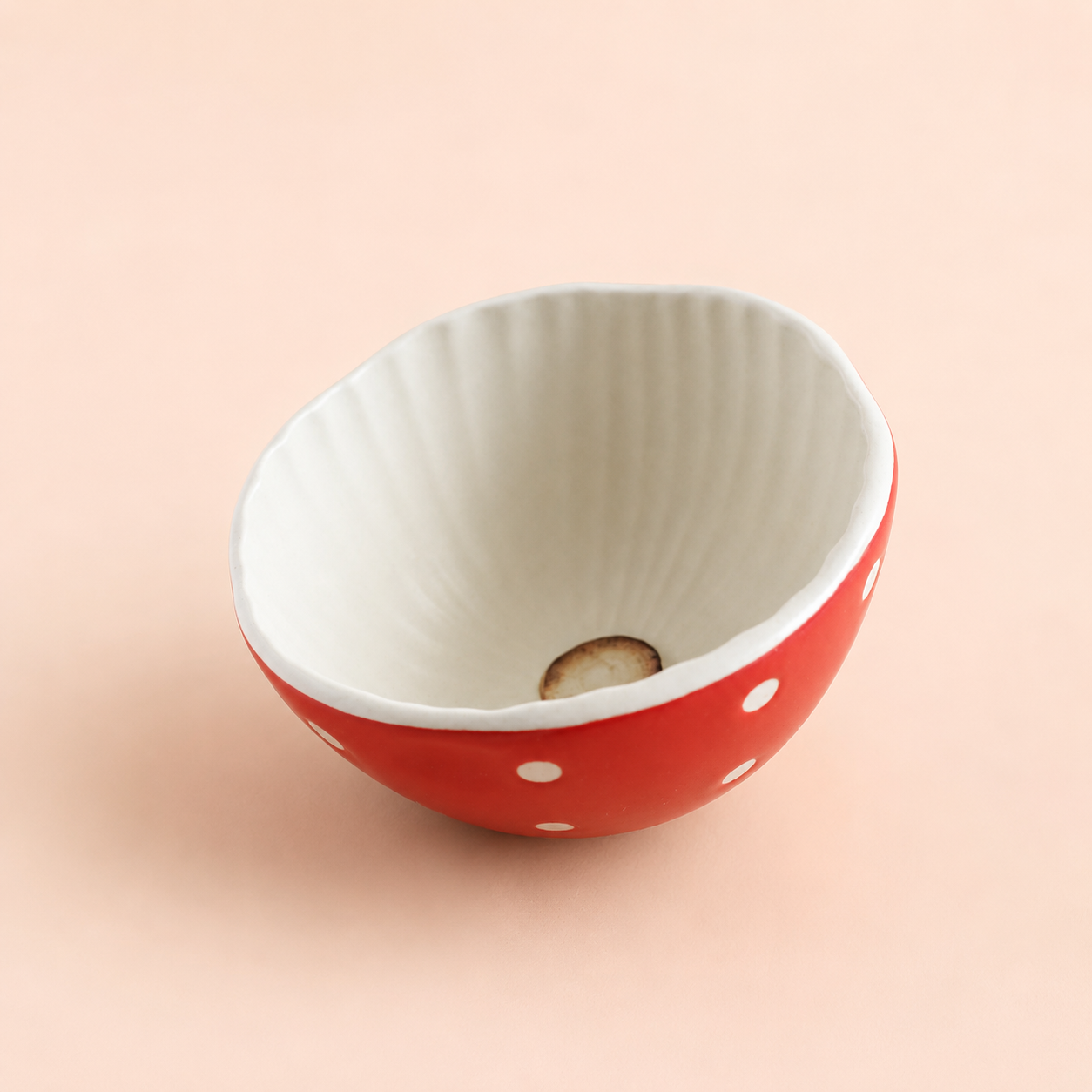 A small ceramic bowl with a red exterior decorated with white polka dots and a ribbed white interior, set against a solid pale peach background.