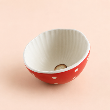 A small ceramic bowl with a red exterior decorated with white polka dots and a ribbed white interior, set against a solid pale peach background.