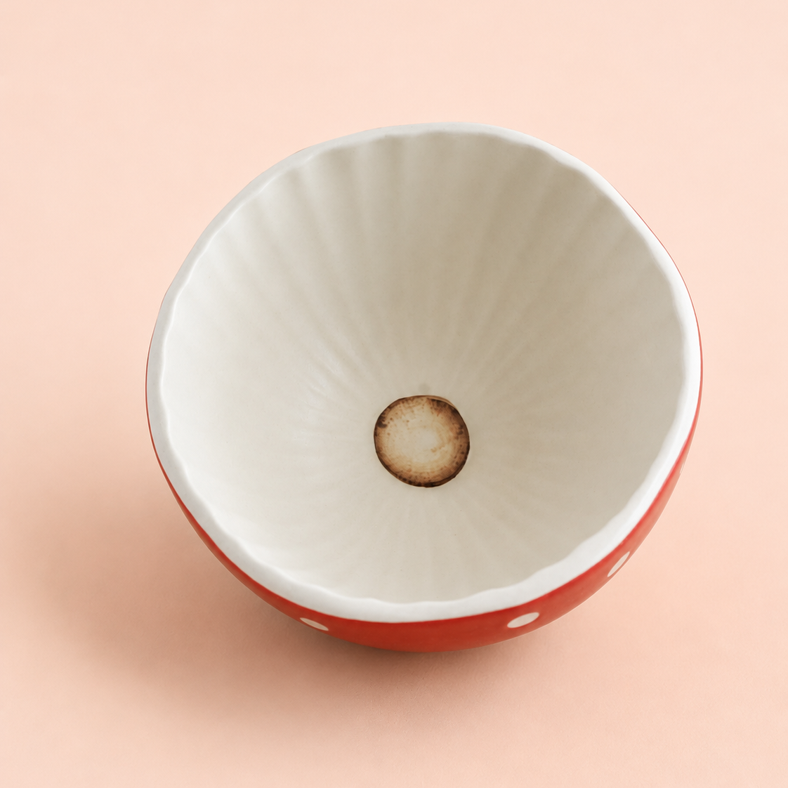 A ceramic bowl viewed from above, featuring a white interior with subtle radial ridges and a warm brown circular detail at the center, set against a solid pale peach background.