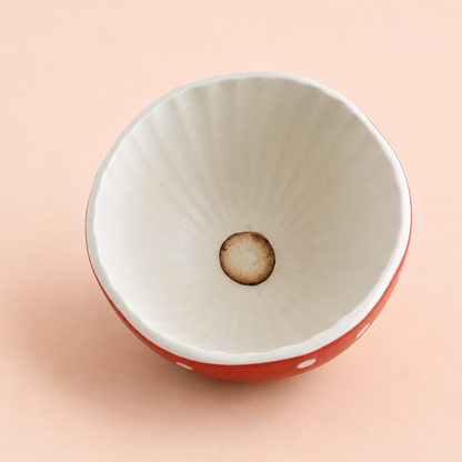 A ceramic bowl viewed from above, featuring a white interior with subtle radial ridges and a warm brown circular detail at the center, set against a solid pale peach background.