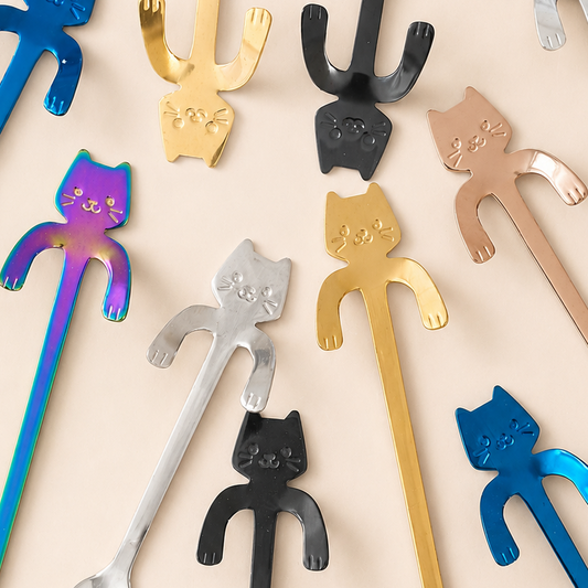 A set of long metal spoons with cat-shaped handles, shown in multiple metallic finishes including blue, gold, black, rose gold, and iridescent, arranged on a light beige background.