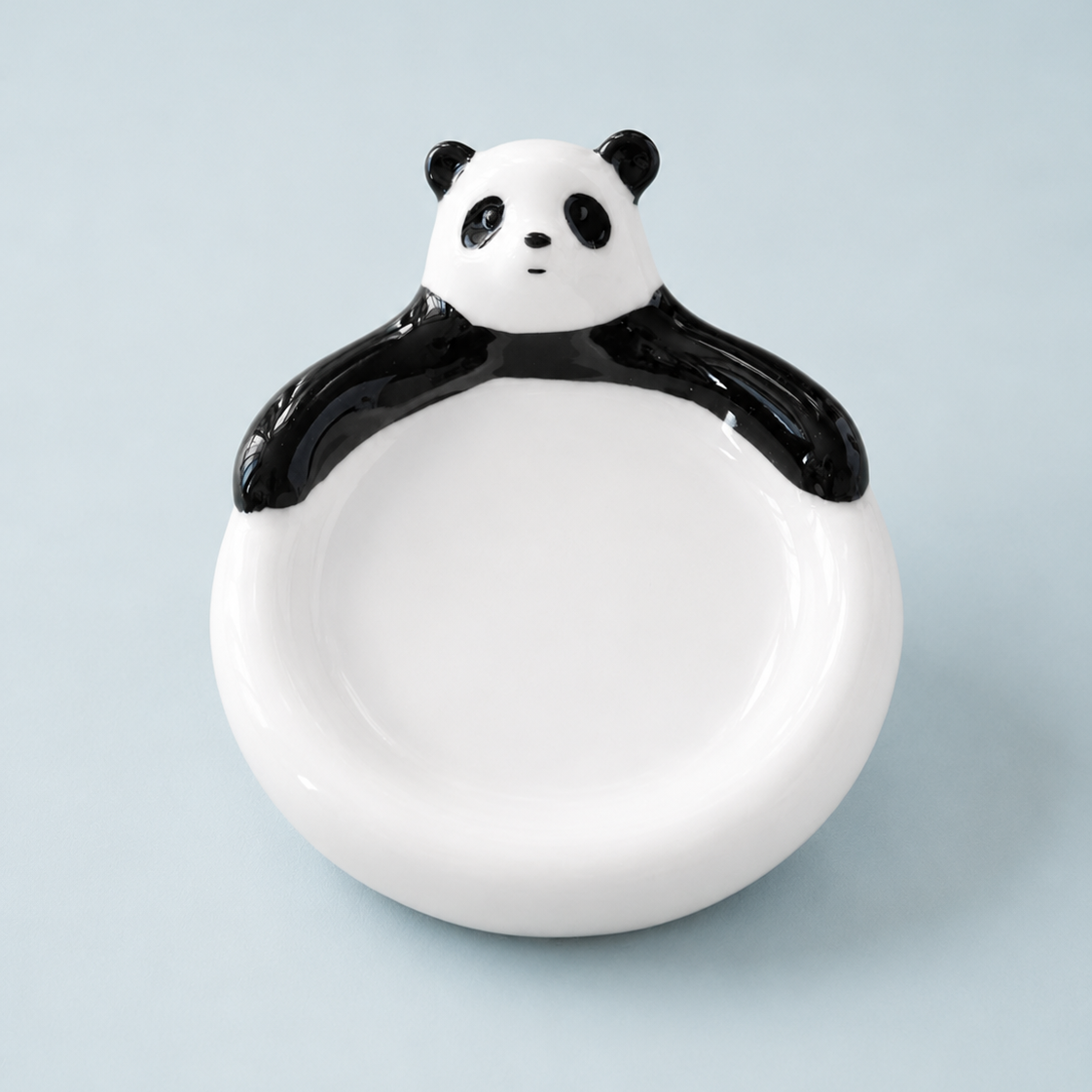 A ceramic panda-shaped dish with a glossy black and white finish, set against a solid light blue background.