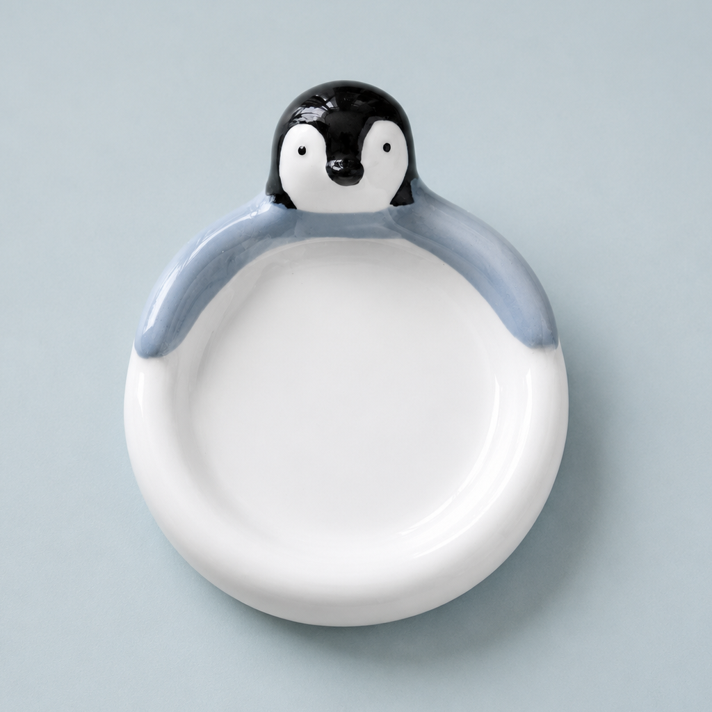 A ceramic penguin-shaped dish with a white bowl and a black-and-white penguin head on a light blue-gray background.
