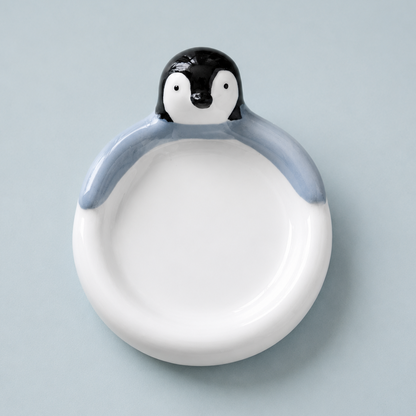 A ceramic penguin-shaped dish with a white bowl and a black-and-white penguin head on a light blue-gray background.
