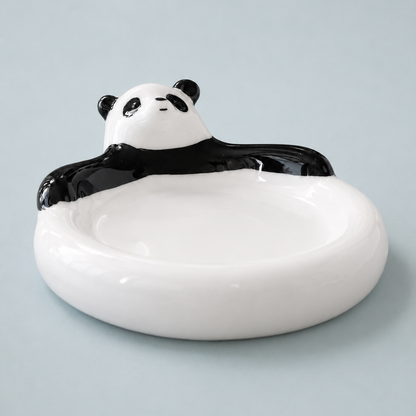 A white ceramic dish with a black-and-white panda design around the rim, photographed on a light blue-gray background.