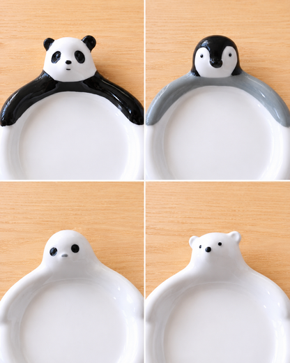 Four ceramic plate designs shown in a 2x2 grid on a light wood background, featuring cartoon animal heads over the rim: panda, penguin, seal, and polar bear.