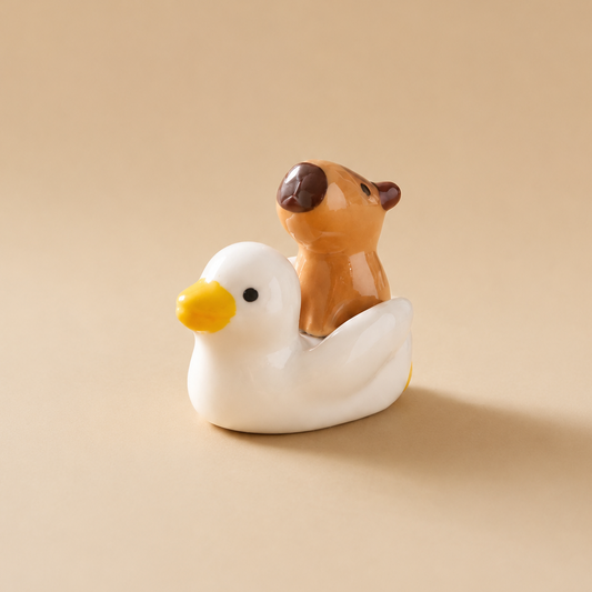 A small ceramic figurine of a white duck carrying a brown capybara, set against a solid beige background.
