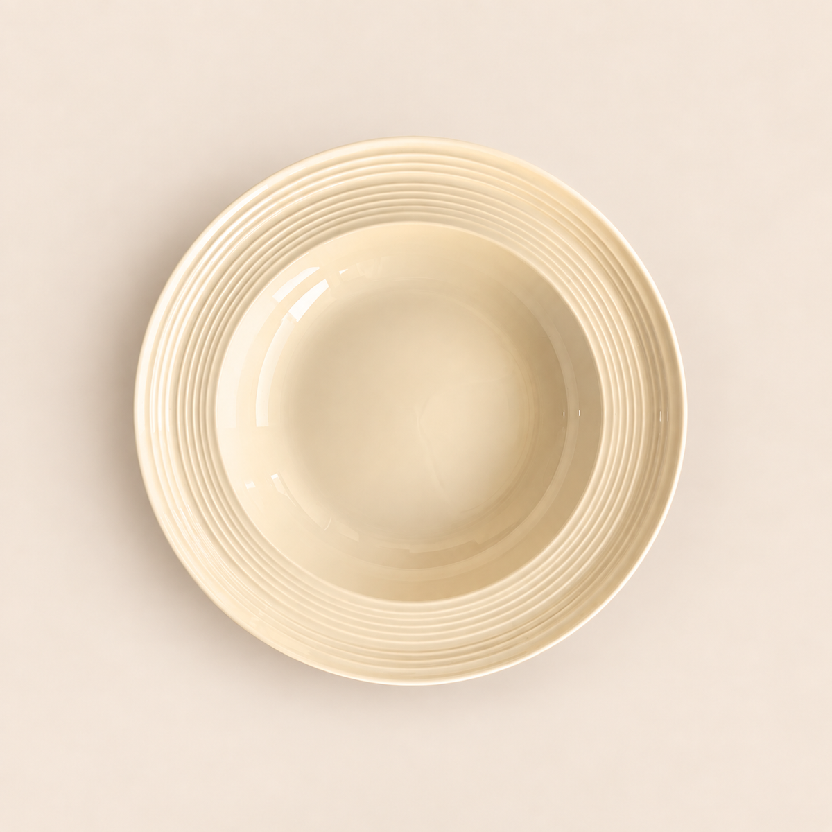 A cream-colored ceramic bowl with a ribbed rim, photographed from a top-down perspective on a matching light beige background.