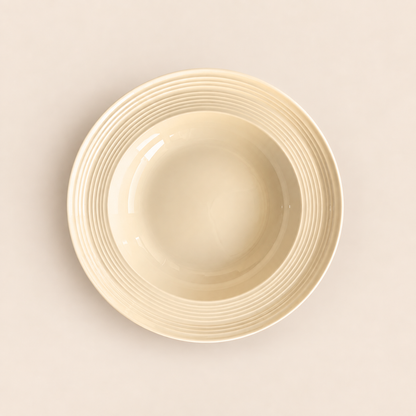 A cream-colored ceramic bowl with a ribbed rim, photographed from a top-down perspective on a matching light beige background.