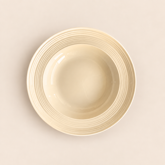 A cream-colored ceramic bowl with a ribbed rim, photographed from a top-down perspective on a matching light beige background.