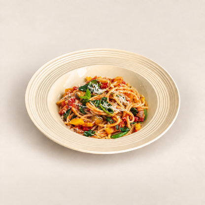 A bowl of spaghetti with tomato sauce, green spinach, and grated cheese, served in a cream-colored ribbed ceramic bowl on a light beige background.