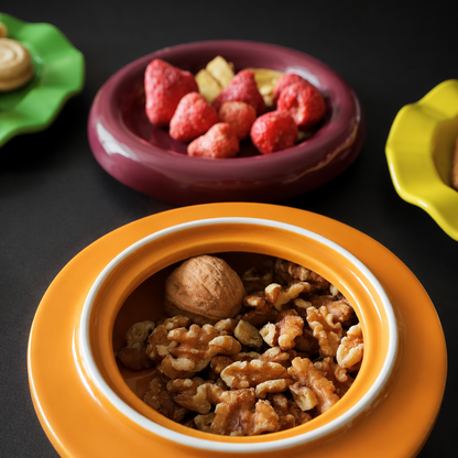 An orange ceramic bowl with a white inner rim, filled with walnuts and a whole nut, set on a dark surface with other colorful bowls in the background.