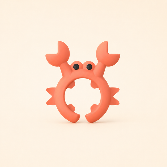 A coral orange crab-shaped Utensil and Lid Holder with small black bead eyes, centered on a warm cream background.