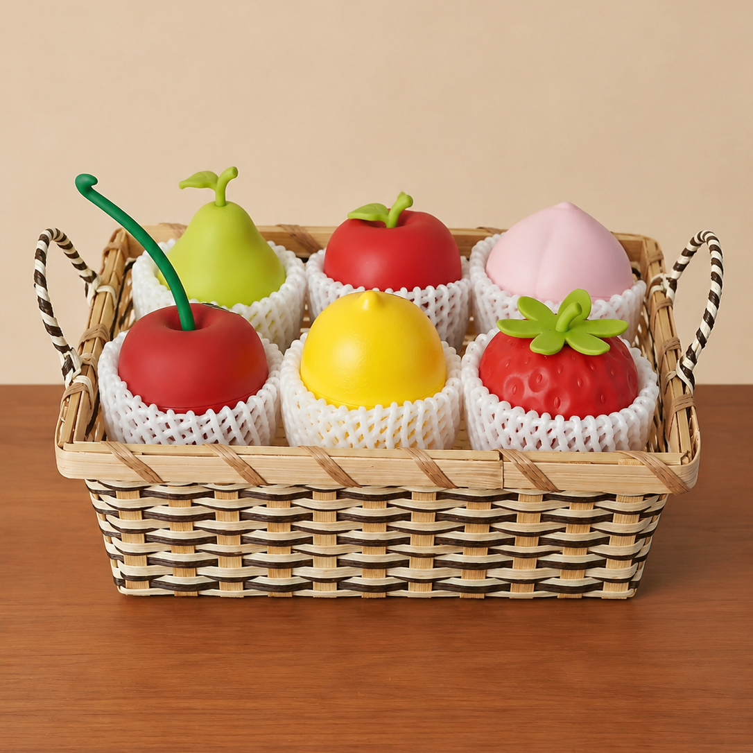 A woven rectangular basket holding six toy fruit-shaped Aromatherapy Set in white mesh sleeves, arranged on a wooden surface against a plain beige background.