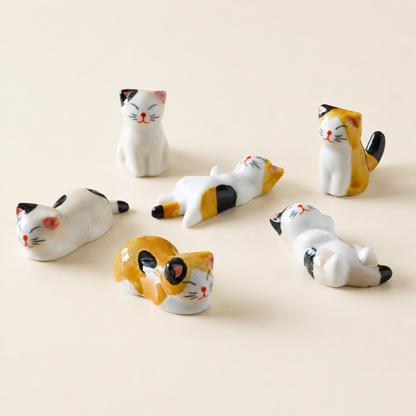 A set of six small ceramic cat figurines in various poses, featuring white, yellow, black, and orange calico patterns, arranged on a light beige background.