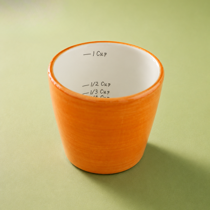 An orange ceramic measuring cup with a white interior printed with cup measure markings, set against a solid light green background.