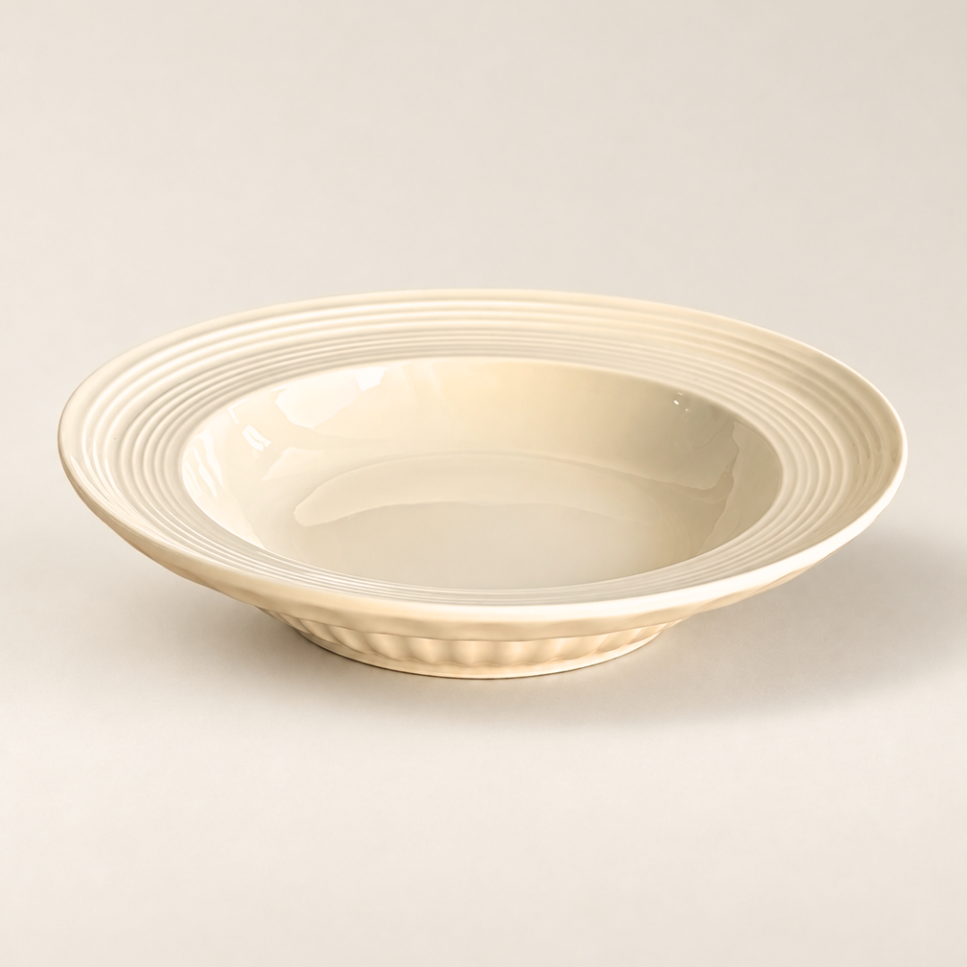 A cream-colored ceramic deep bowl with concentric ring patterns on the rim and a fluted base, photographed on a neutral light beige background.