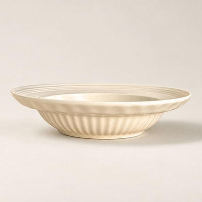 An off-white ceramic bowl with a fluted, ribbed exterior and a smooth, slightly tapered interior, shown on a neutral light beige background.