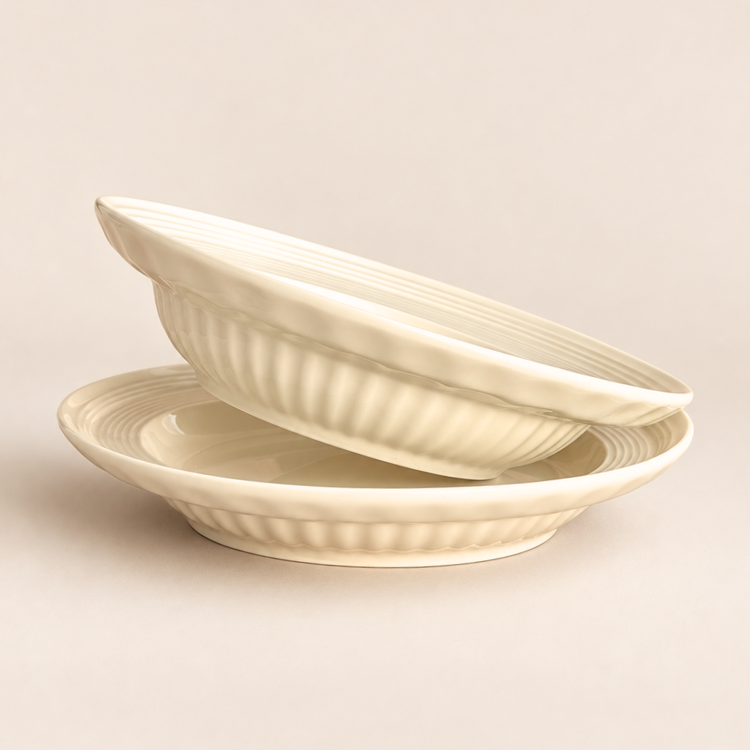 Two cream-colored ceramic bowls with a ribbed fluted exterior, stacked on a matching saucer against a solid light beige background.