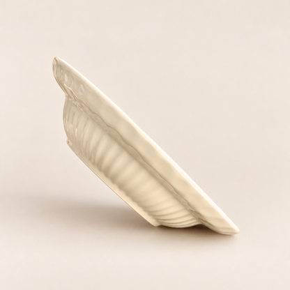 An off-white ceramic plate with a ribbed leaf-like pattern, shown from an angled side view on a solid, warm beige background.